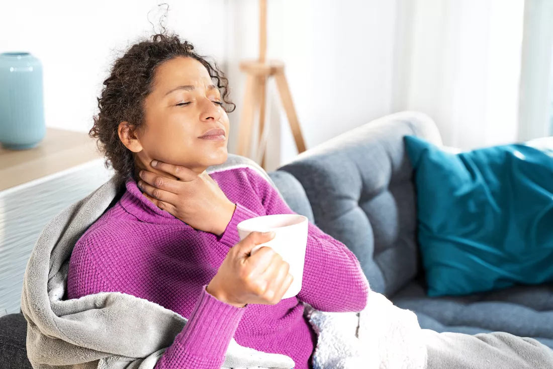 woman rubs sore throat and drinks tea